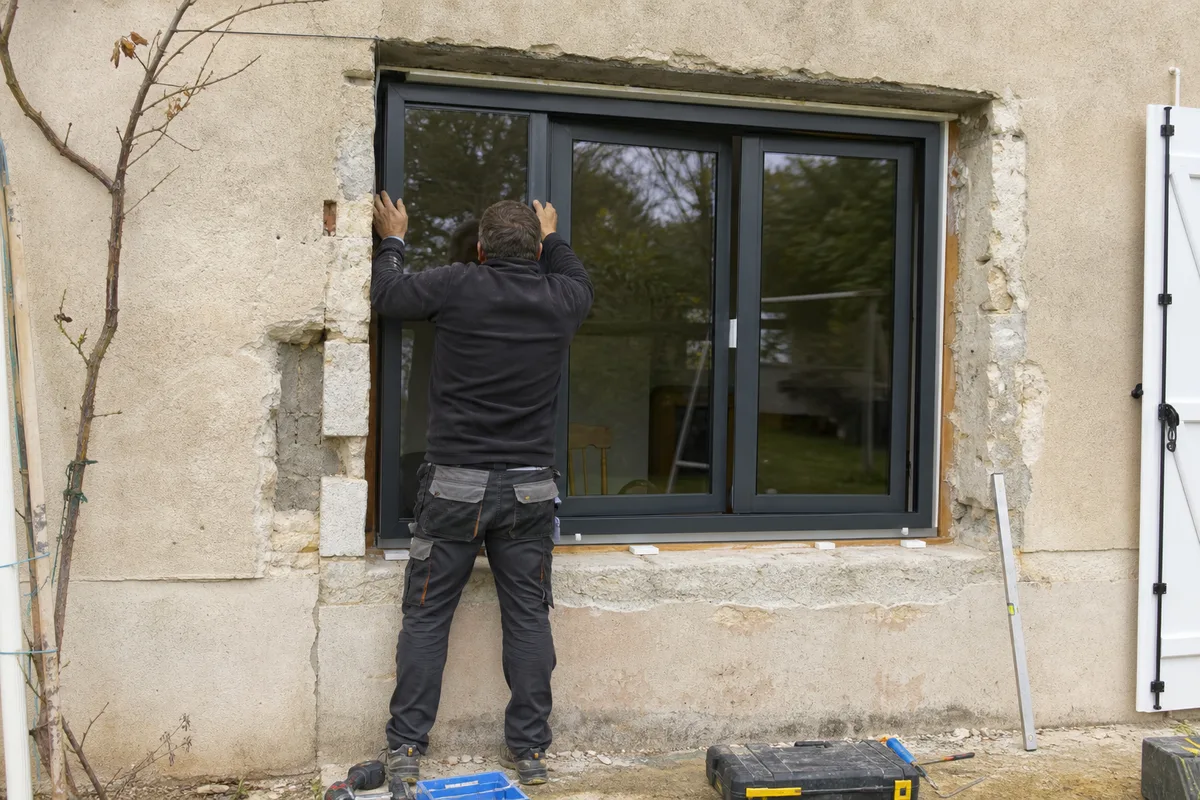 Installateur ajustant un châssis de fenêtre aluminium avant la pose, vu depuis l’extérieur
